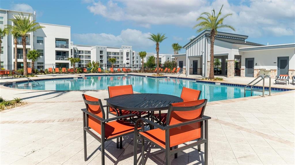 A round patio table with four orange chairs sits on a pool deck outdoors — 4741 CLOCK TOWER DRIVE UNIT 102, KISSIMMEE, FL