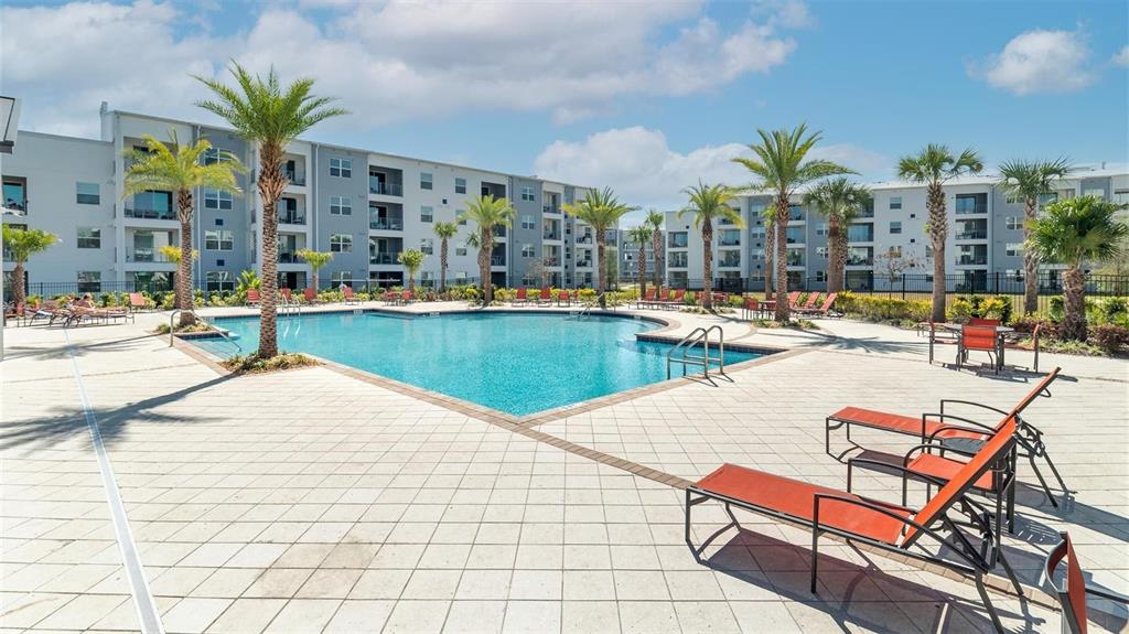 A swimming pool surrounded by lounge chairs and palm trees in front of apartment buildings — 4741 CLOCK TOWER DRIVE UNIT 102, KISSIMMEE, FL