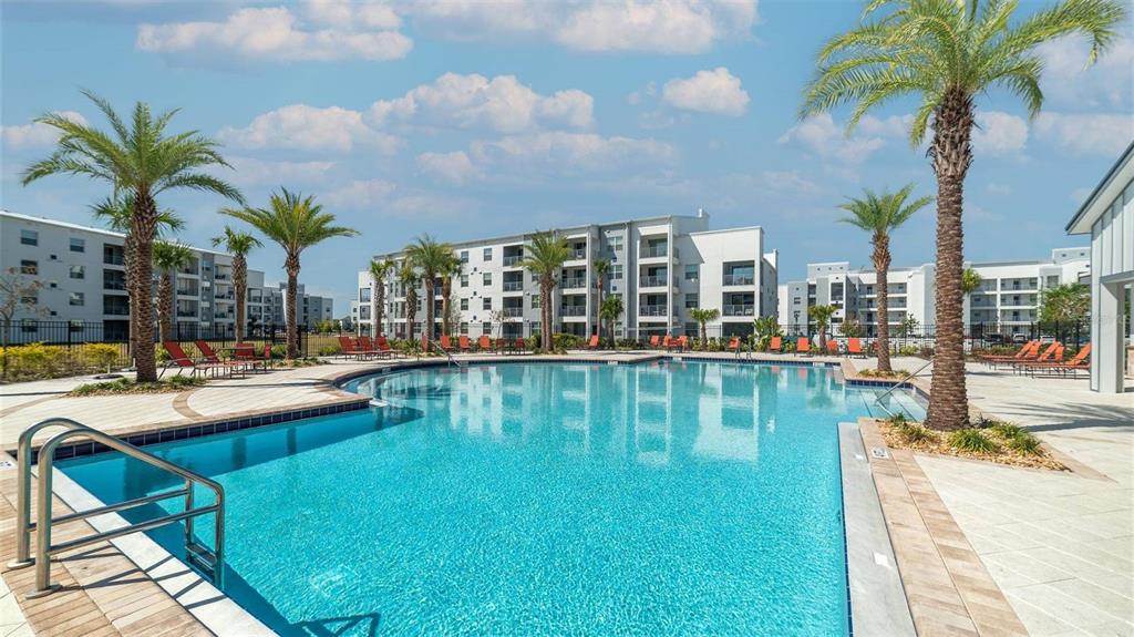 A swimming pool sits in the courtyard of a multi-story apartment complex with palm trees — 4741 CLOCK TOWER DRIVE UNIT 102, KISSIMMEE, FL