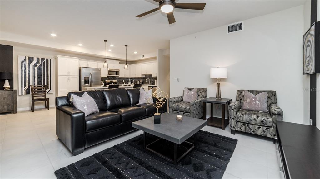 A living room with a black leather sofa, patterned armchairs, and an open-concept kitchen — 4741 CLOCK TOWER DRIVE UNIT 102, KISSIMMEE, FL
