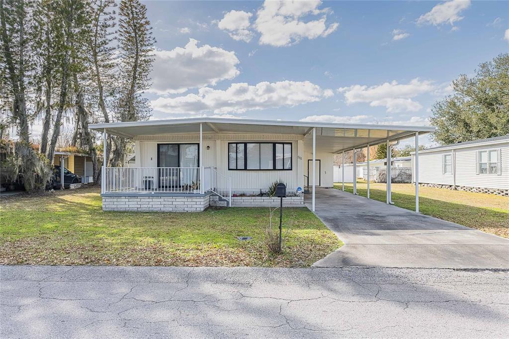 A single-story manufactured home with a white exterior, front porch, and attached carport — 511 LAZY LAKE DRIVE W, LAKELAND, FL