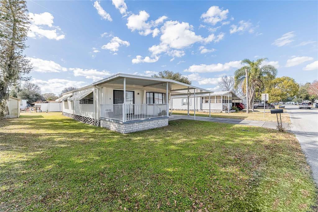 A single-story manufactured home with a covered front porch and carport sits on a lawn — 511 LAZY LAKE DRIVE W, LAKELAND, FL