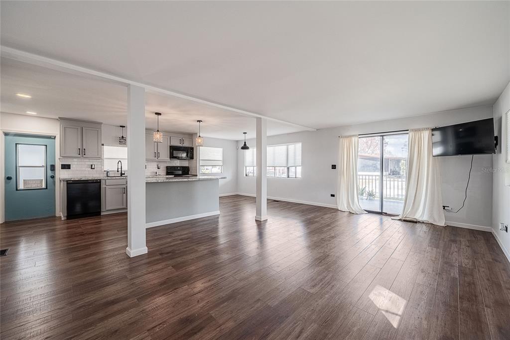 An open-concept living area features wood-look flooring, a kitchen with gray cabinets, and sliding doors — 511 LAZY LAKE DRIVE W, LAKELAND, FL