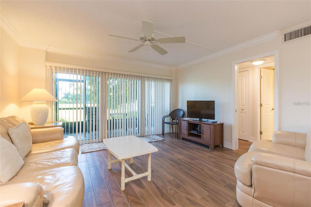 A living room features light-colored leather sofas, a white coffee table, and wood-look flooring — 5642 PUERTA DEL SOL BOULEVARD S UNIT 142, ST PETERSBURG, FL
