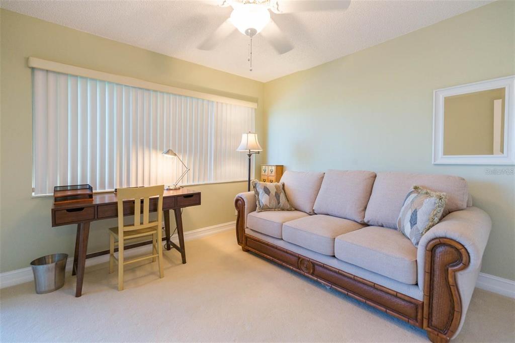 A room with a beige sofa, a wooden desk, and a ceiling fan — 5642 PUERTA DEL SOL BOULEVARD S UNIT 142, ST PETERSBURG, FL
