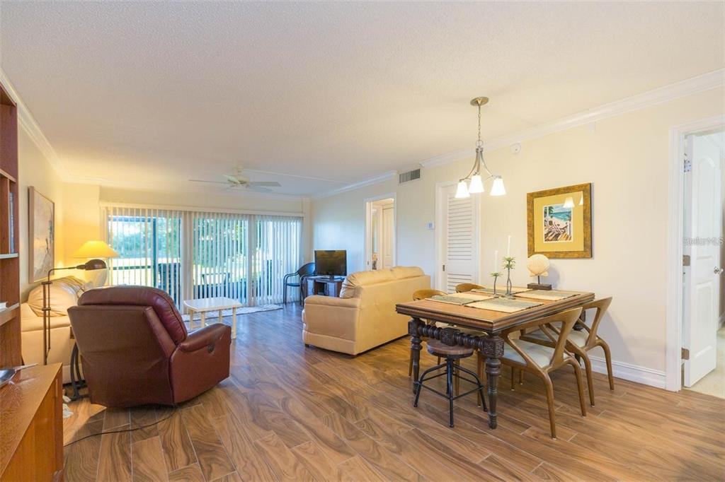 A living and dining area with wood-look flooring, a red recliner, and a beige sofa — 5642 PUERTA DEL SOL BOULEVARD S UNIT 142, ST PETERSBURG, FL