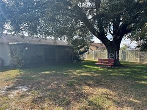 A backyard features a large tree, a red bench, and a screened-in porch — 746 MADERIA COURT, KISSIMMEE, FL