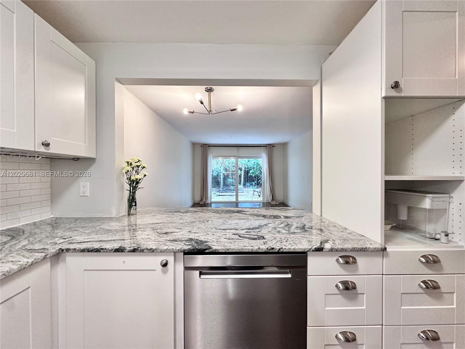 A kitchen with white cabinets and granite countertops overlooks a living area with sliding doors — 9974 SW 88th St # 1016, Miami FL 33176, MIAMI, FL