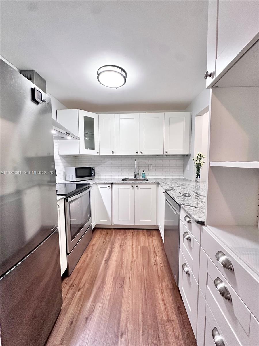A galley kitchen features white cabinets, stainless steel appliances, and granite countertops — 9974 SW 88th St # 1016, Miami FL 33176, MIAMI, FL