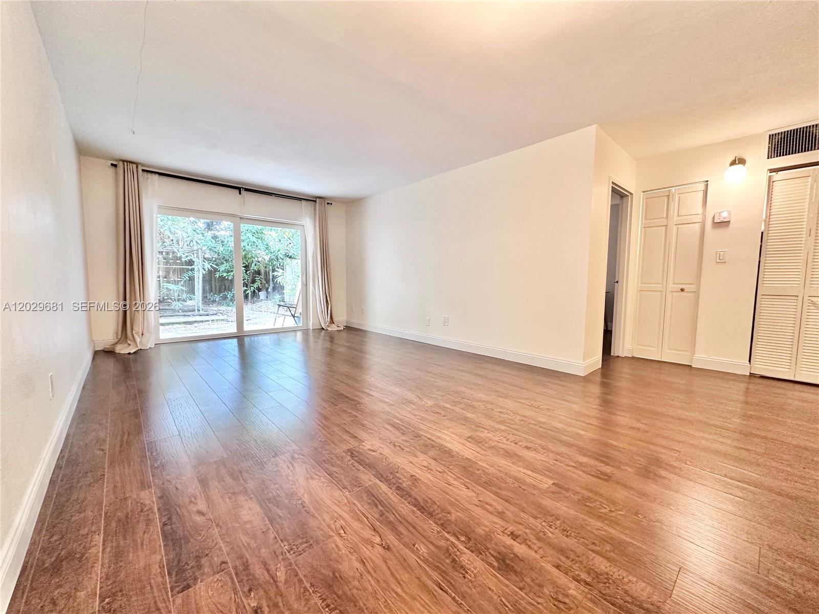 An empty living room features wood-look flooring, white walls, and sliding glass doors to a patio — 9974 SW 88th St # 1016, Miami FL 33176, MIAMI, FL