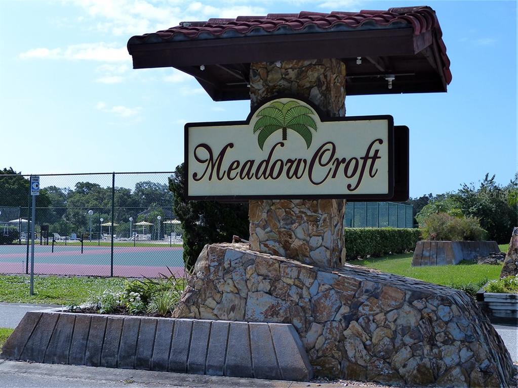 A stone monument sign for Meadow Croft stands in front of a fenced tennis court — 1403 56TH STREET W UNIT 1403, BRADENTON, FL