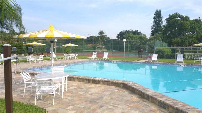 A swimming pool with a yellow umbrella table and tennis courts in the background — 1403 56TH STREET W UNIT 1403, BRADENTON, FL