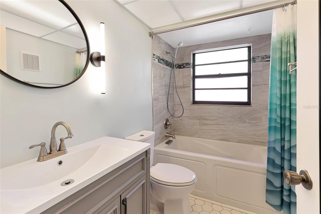 A bathroom features a gray vanity, a round mirror, a toilet, and a tiled bathtub — 1403 56TH STREET W UNIT 1403, BRADENTON, FL