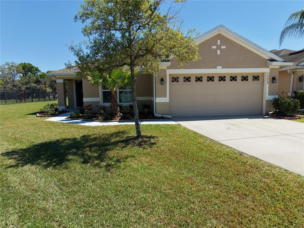 A single-story tan house with a two-car garage and a front yard with a tree — 15637 CARINA DR, ORLANDO, FL