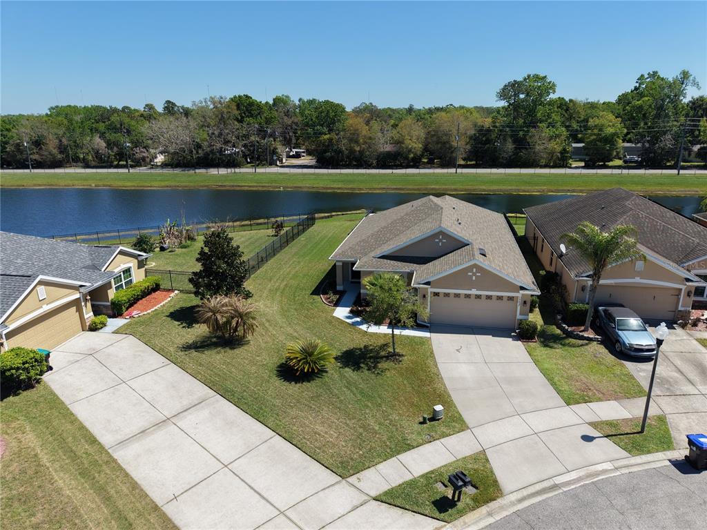 An aerial view shows three suburban houses with driveways and lawns bordering a small lake — 15637 CARINA DR, ORLANDO, FL