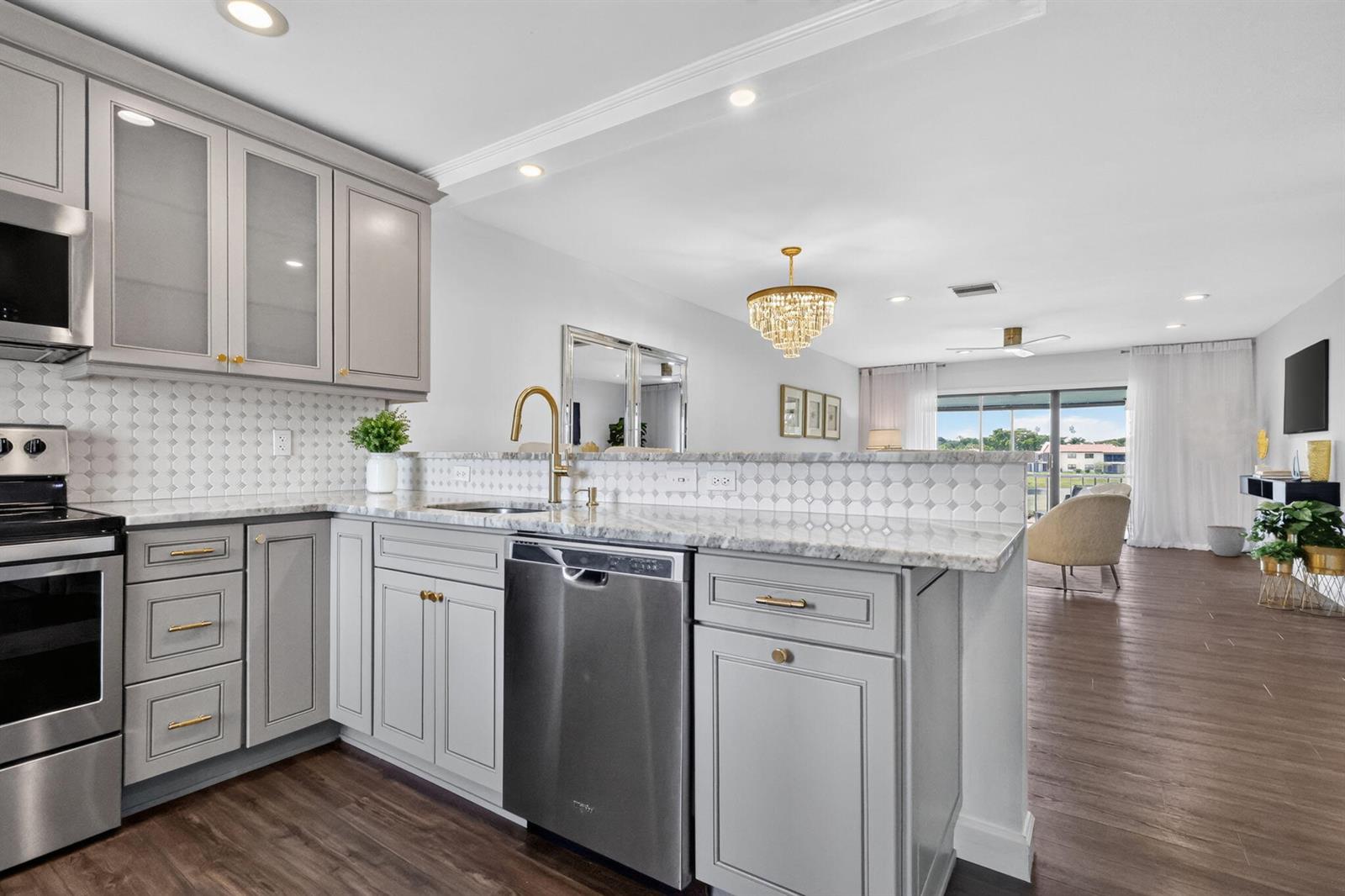 A kitchen with gray cabinets, marble countertops, and a gold faucet overlooks a living area — 21219 Lago Circle # 5j, Boca Raton FL 33433, BOCA RATON, FL