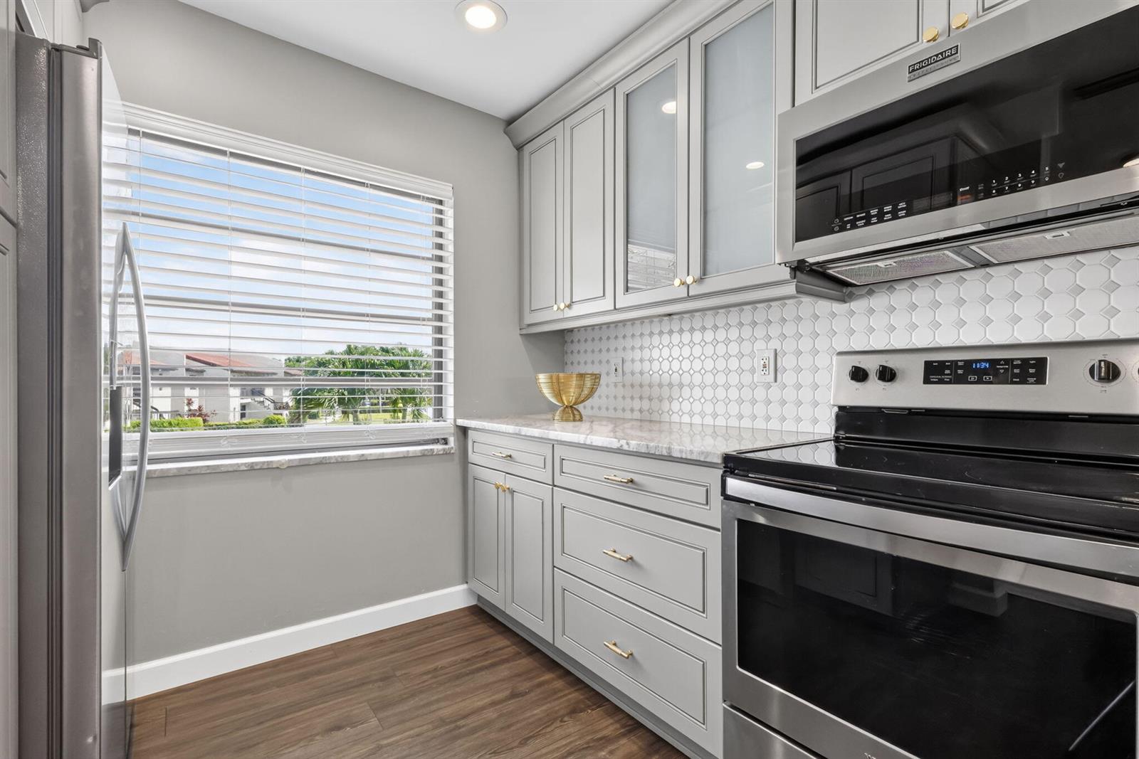 A kitchen features grey cabinets, a marble countertop, a tiled backsplash, and stainless steel appliances — 21219 Lago Circle # 5j, Boca Raton FL 33433, BOCA RATON, FL