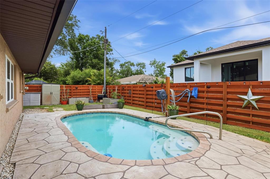 A backyard features an oval swimming pool with stone decking and a horizontal wood fence — 541 MORNINGSIDE ROAD, VENICE, FL