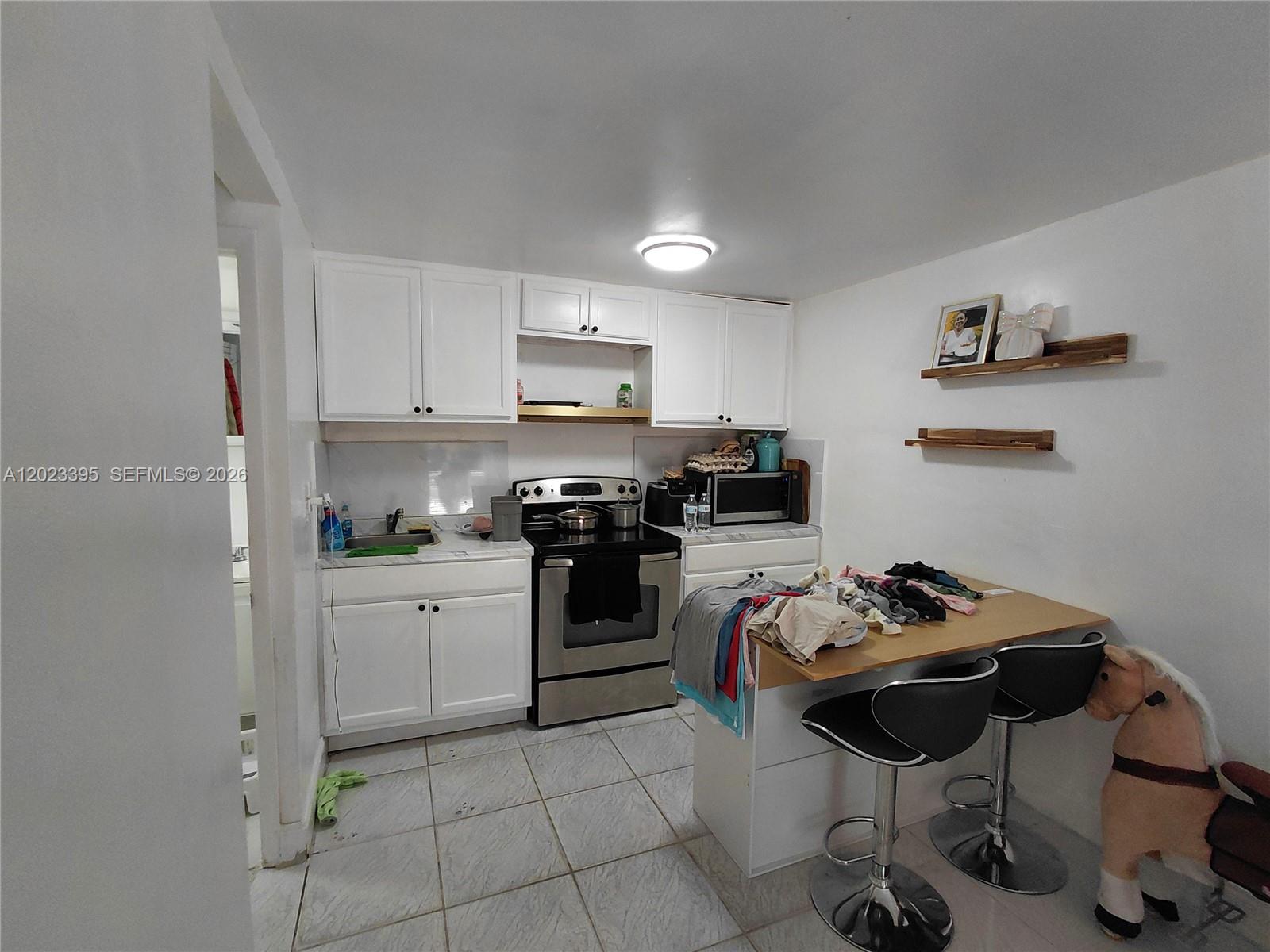 A small kitchen features white cabinets, stainless steel appliances, a breakfast bar, and tiled flooring — 2140 NW 1st Ter, Miami FL 33125, MIAMI, FL