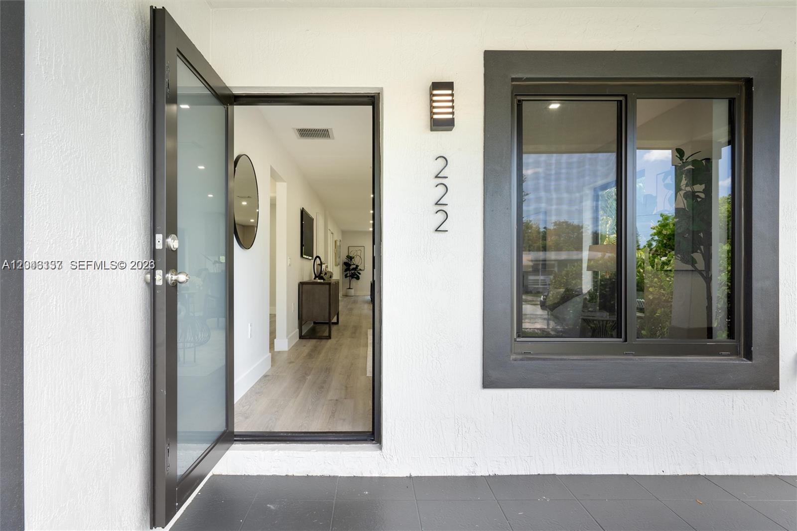 An open front door reveals a modern interior hallway with light wood flooring — 222 SW 3rd Ter, Dania Beach FL 33004, DANIA BEACH, FL