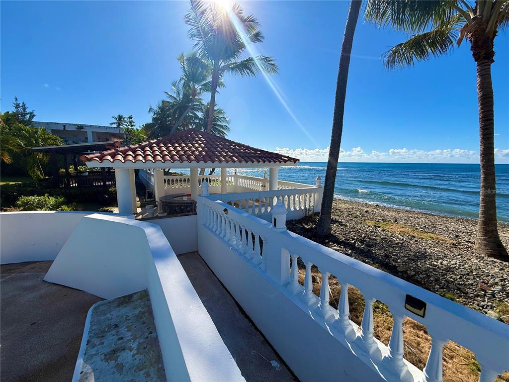 A white balustrade overlooks a stone beach and a gazebo by the ocean — Carr #3 BEACH FRONT GUEST HOUSE, PATILLAS, PR