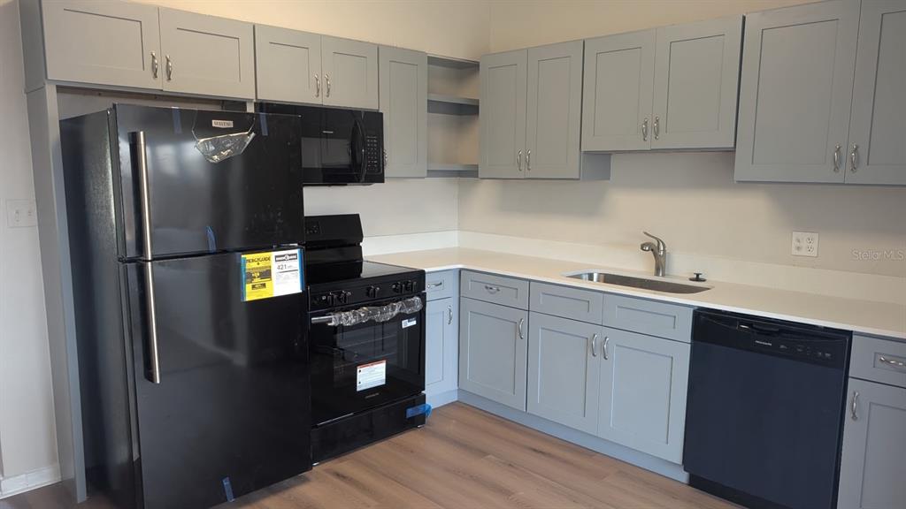 A kitchen features grey cabinets, black appliances, a stainless steel sink, and light wood flooring — 714 GOVERNORS AVENUE, ORLANDO, FL