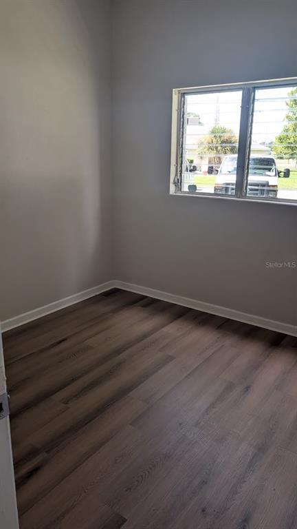 An empty room with light gray walls, wood-look flooring, and a window with security bars — 714 GOVERNORS AVENUE, ORLANDO, FL