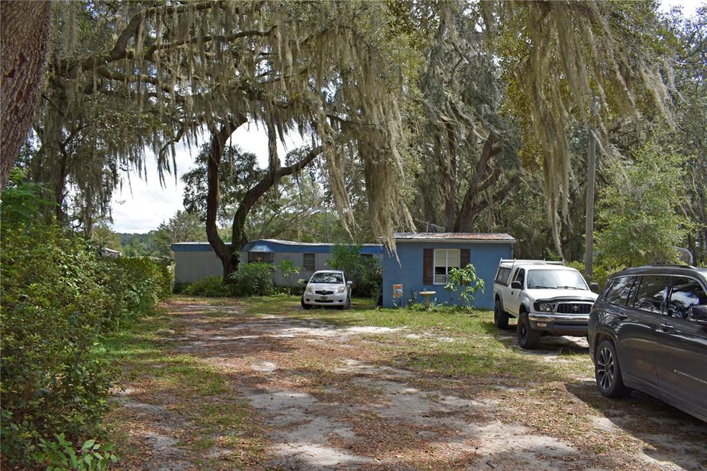 A blue mobile home sits on a dirt lot shaded by large, moss-covered oak trees — 148 SWAN LAKE DRIVE, MELROSE, FL