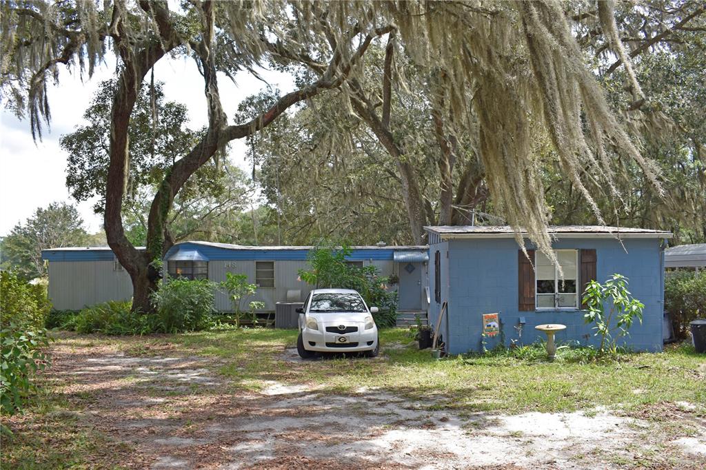 A mobile home with an attached blue structure sits under large trees with Spanish moss — 148 SWAN LAKE DRIVE, MELROSE, FL