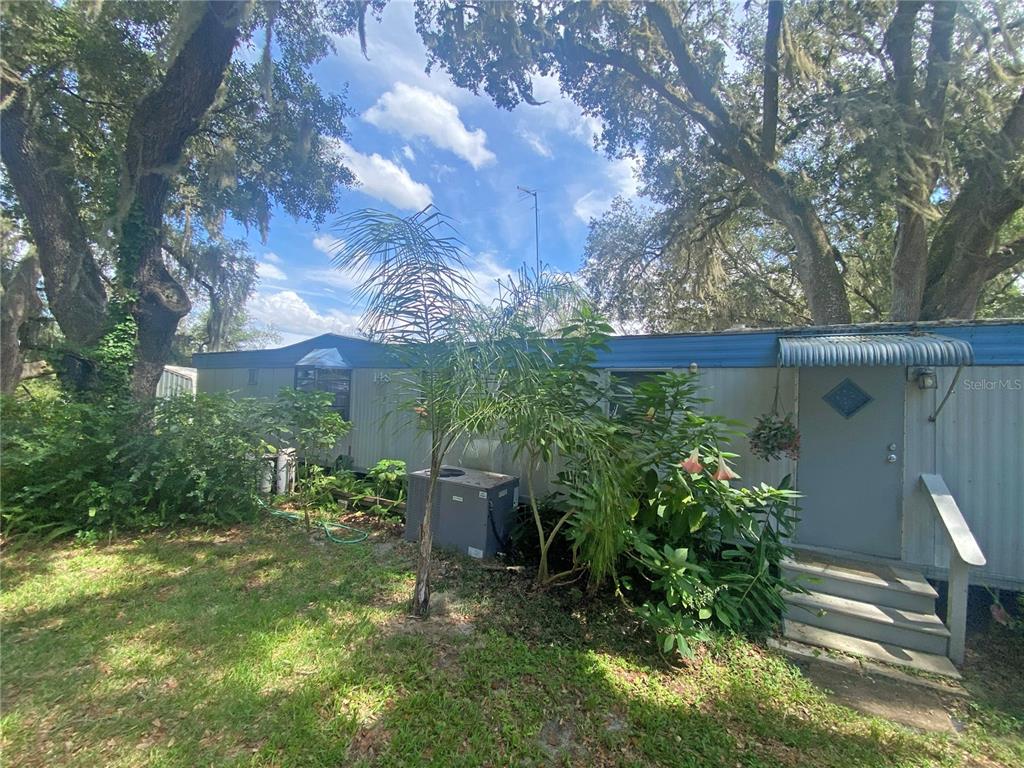 A mobile home exterior features a gray door, metal awning, and surrounding trees and plants — 148 SWAN LAKE DRIVE, MELROSE, FL