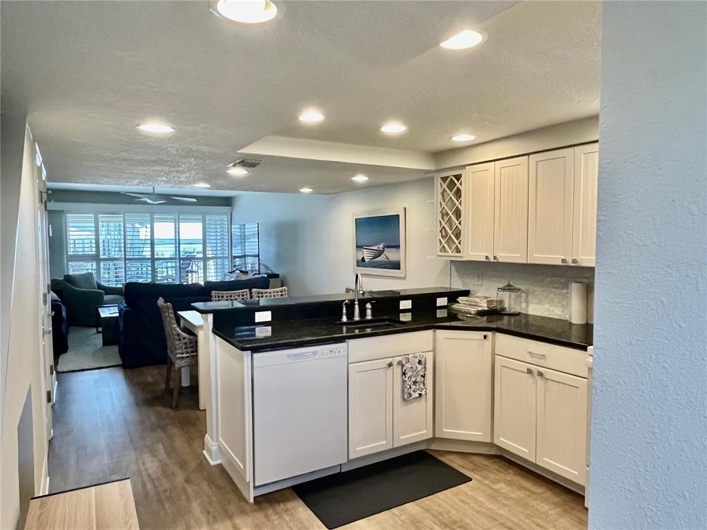 A kitchen with white cabinets and black countertops opens into a living area with shutters — 2100 N PENINSULA AVENUE UNIT 2160, NEW SMYRNA BEACH, FL