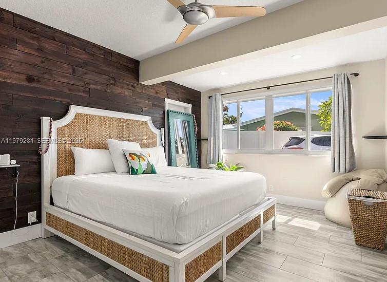 A bedroom features a wicker bed frame, a dark wood accent wall, and light tile flooring — 2211 NE 35th Ct, Lighthouse Point FL 33064, LIGHTHOUSE POINT, FL