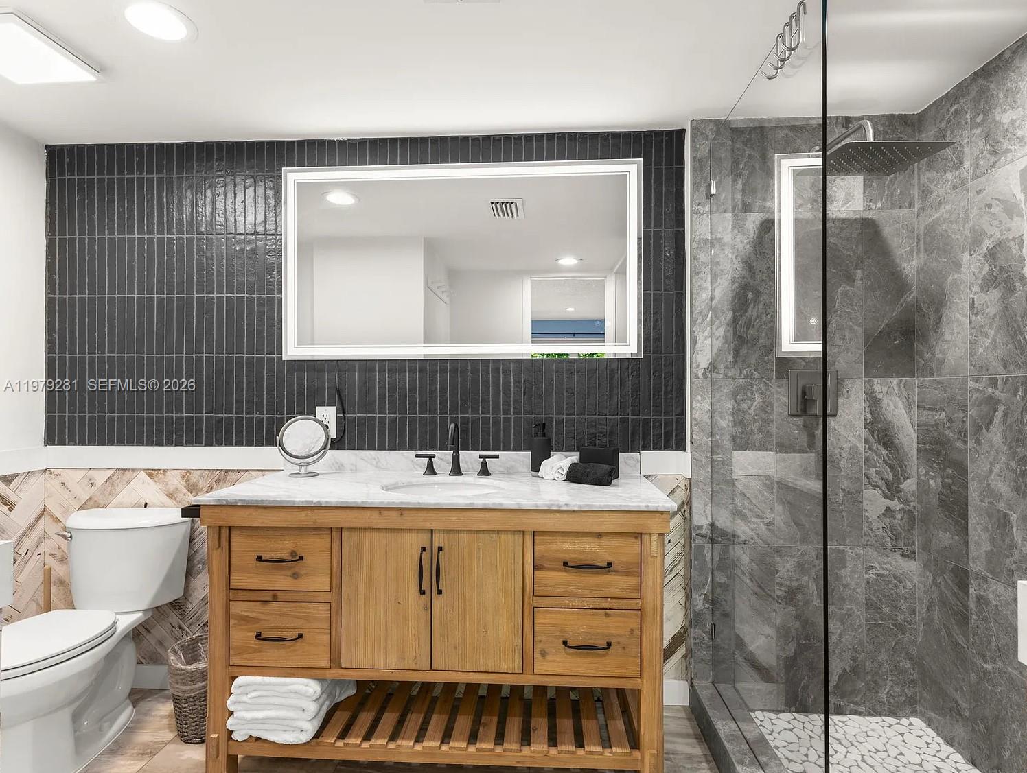 A bathroom features a wooden vanity, a marble countertop, and a glass-enclosed walk-in shower — 2211 NE 35th Ct, Lighthouse Point FL 33064, LIGHTHOUSE POINT, FL