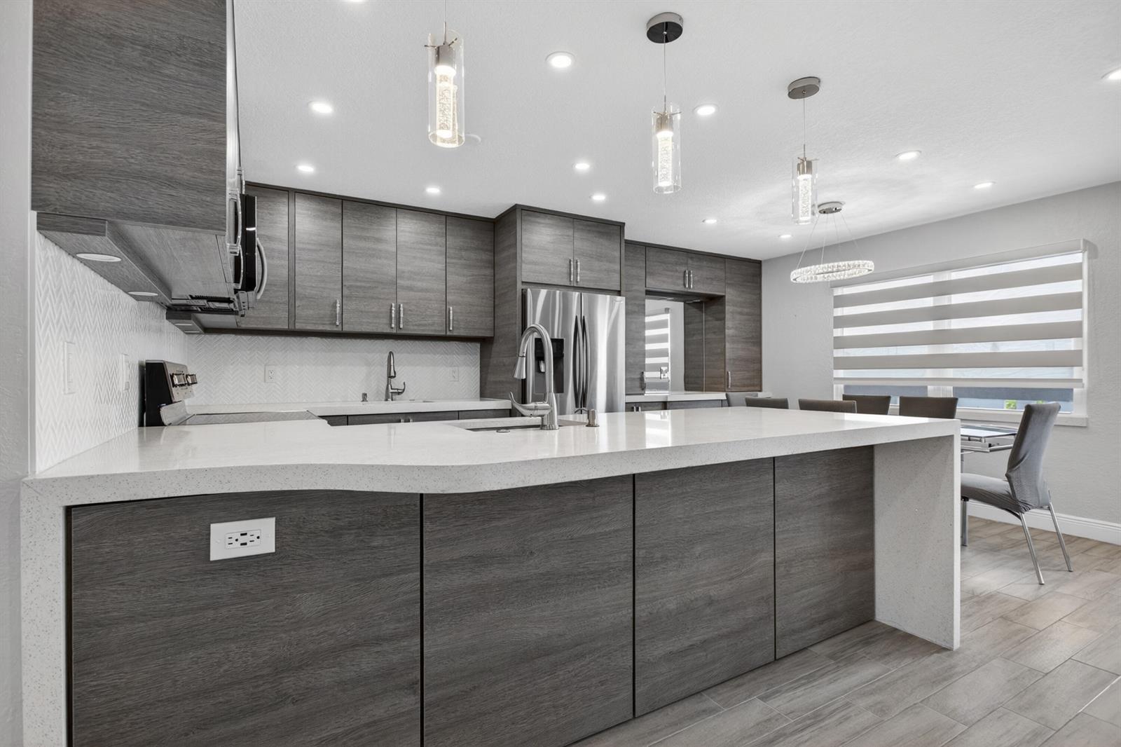 A modern kitchen features dark wood cabinetry, white quartz countertops, and a large center island — 446 Richmond F, Deerfield Beach FL 33442, DEERFIELD BEACH, FL