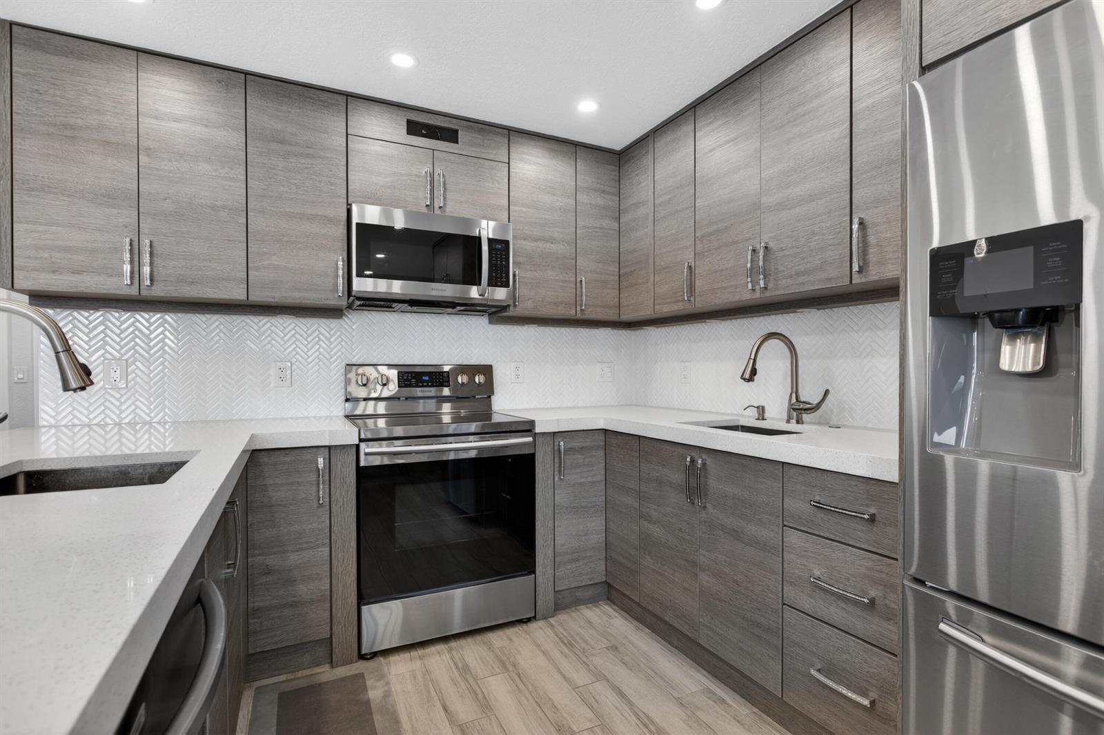A modern kitchen features grey wood-grain cabinets, stainless steel appliances, and white quartz countertops — 446 Richmond F, Deerfield Beach FL 33442, DEERFIELD BEACH, FL