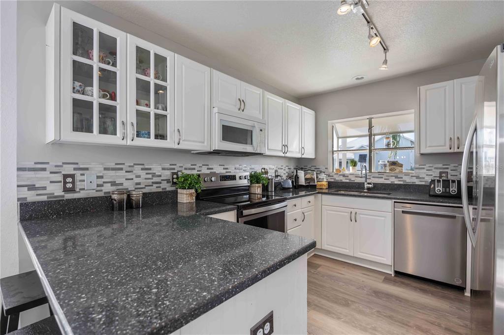 A kitchen features white cabinets, dark speckled countertops, stainless steel appliances, and a tiled backsplash — 13951 HARBOR VIEW DRIVE, SEMINOLE, FL