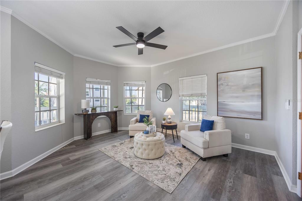 A living room features light gray walls, wood-look flooring, two armchairs, a tufted ottoman, and windows — 13951 HARBOR VIEW DRIVE, SEMINOLE, FL