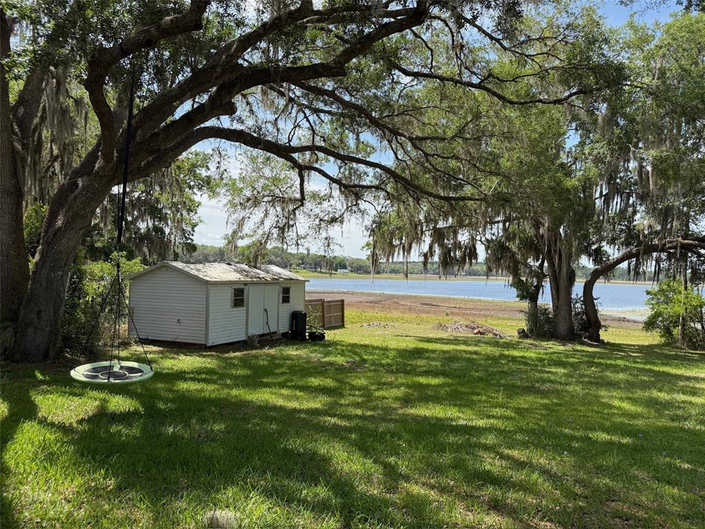A white shed sits on a grassy lawn under large trees overlooking a lake — 3824 SW SHOREWOOD DRIVE, DUNNELLON, FL