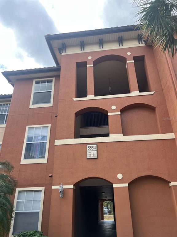 A three-story stucco apartment building features arched entryways and a central unit number sign — 5554 METROWEST BOULEVARD UNIT 4-310, ORLANDO, FL