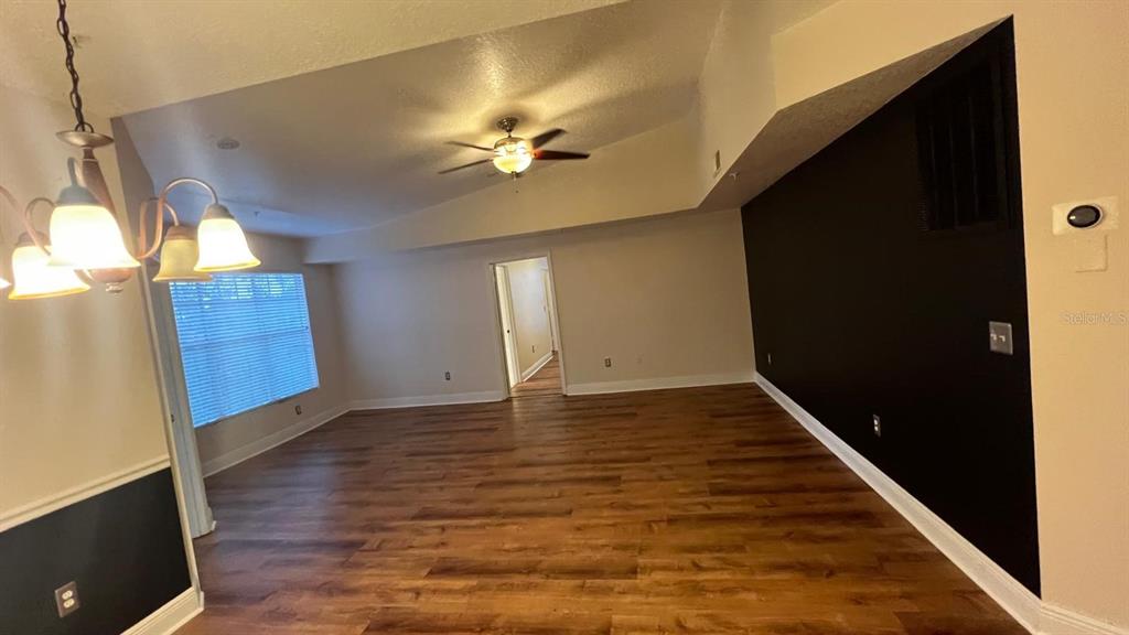 An empty room features wood-look flooring, a vaulted ceiling with a fan, and black walls — 5554 METROWEST BOULEVARD UNIT 4-310, ORLANDO, FL