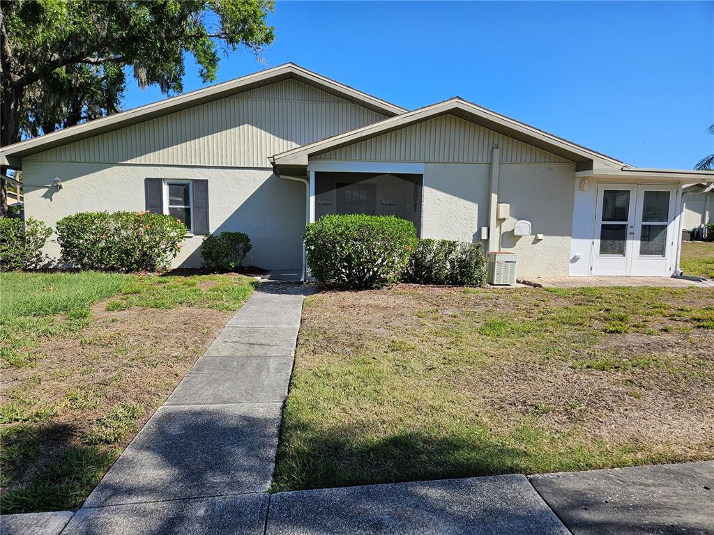 A covered entryway features a tan door, textured walls, and a carpeted ledge with decor — 1905 CANTERBURY LANE UNIT E-9, SUN CITY CENTER, FL