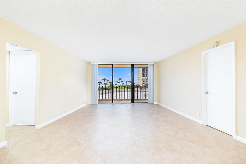 An empty room with beige tile flooring, two white doors, and a balcony overlooking palm trees — 400 Ocean Trail Way # 203, Jupiter FL 33477, JUPITER, FL