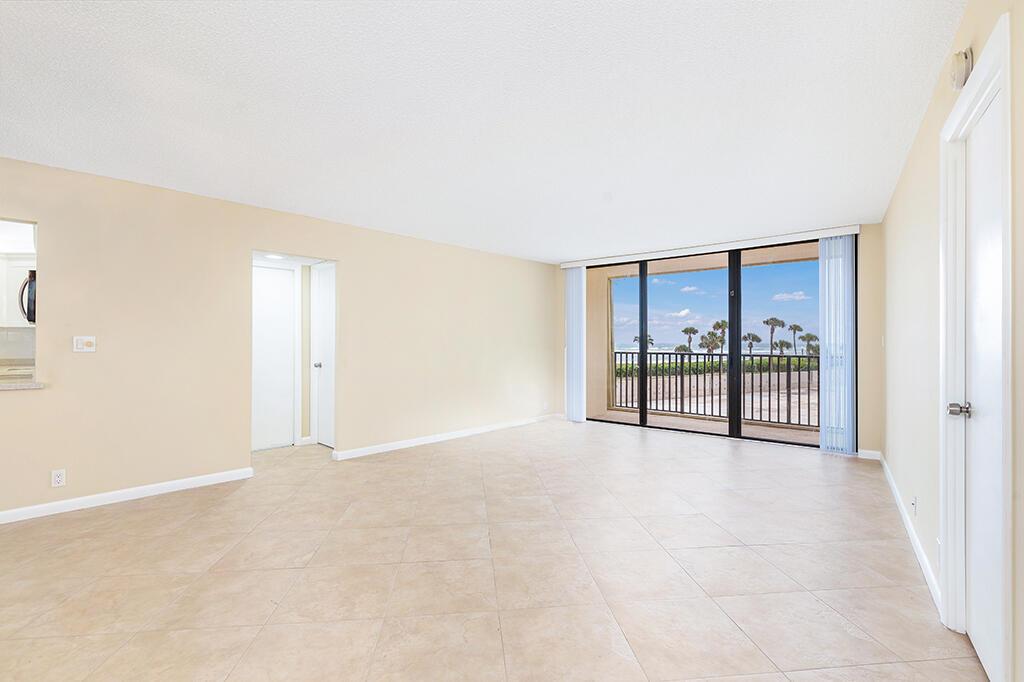 An empty living room with beige tile floors, light walls, and a sliding glass door balcony — 400 Ocean Trail Way # 203, Jupiter FL 33477, JUPITER, FL