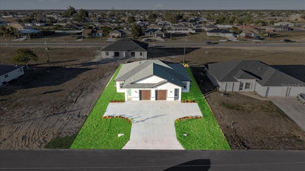 An aerial view shows a newly constructed duplex with a concrete driveway and landscaped lawn — 826/828 DIPLOMAT PARKWAY E, CAPE CORAL, FL