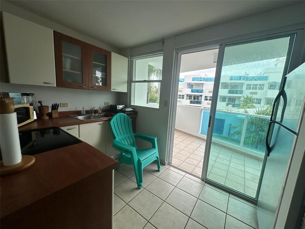 A kitchen with wood-tone cabinets, tile flooring, and a sliding glass door leading to a balcony — Km 7 EL CHARLIE UNIT NE204, LOIZA, PR