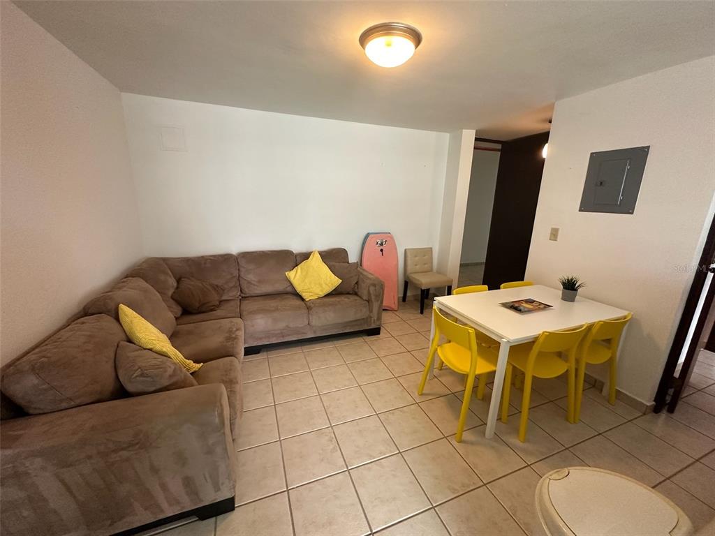 A living and dining area with a brown sectional sofa, white table, and yellow chairs — Km 7 EL CHARLIE UNIT NE204, LOIZA, PR