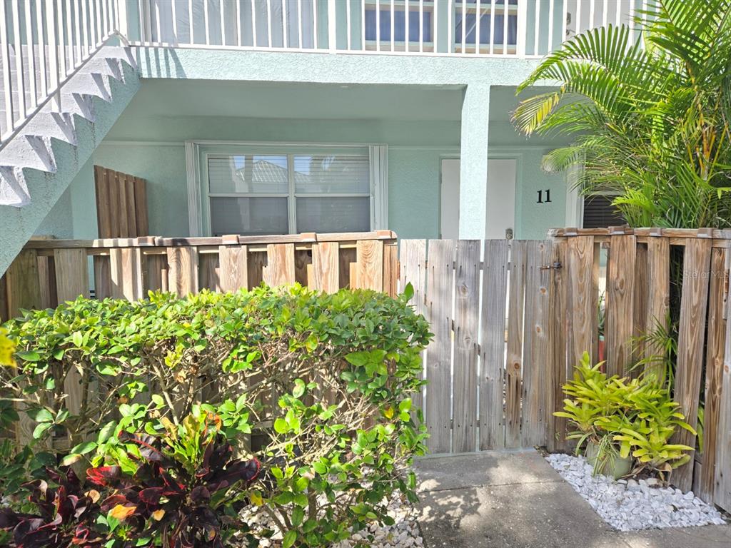 A ground-level apartment entrance features a wooden privacy fence, a small patio, and landscaping — 7605 RIDGEWOOD AVENUE UNIT 11-1, CAPE CANAVERAL, FL