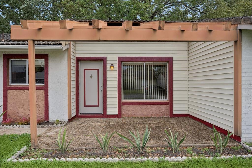 A house exterior features a gravel patio, a wooden pergola, and a beige siding facade — 10113 MUSKET LANE, ORLANDO, FL