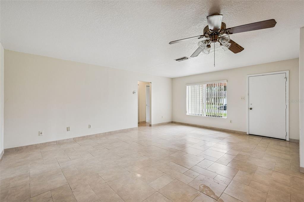An empty living room features light-colored tile flooring, white walls, a ceiling fan, and a door — 10113 MUSKET LANE, ORLANDO, FL