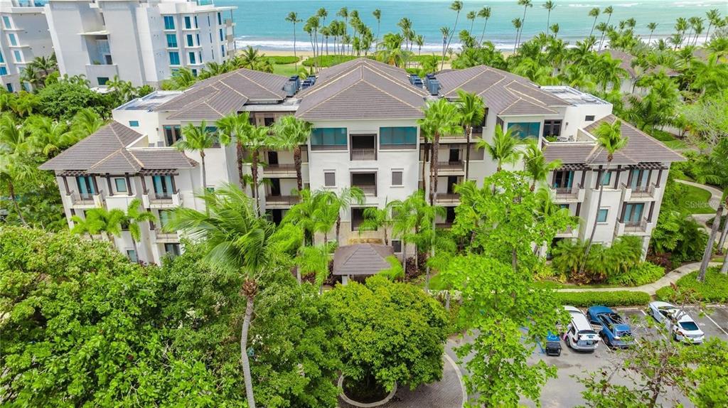 An aerial view shows a multi-story resort building surrounded by lush trees near the ocean — Ventanas II Condominium 7000 BAHIA BEACH BOULEVARD UNIT 313, RIO GRANDE, PR